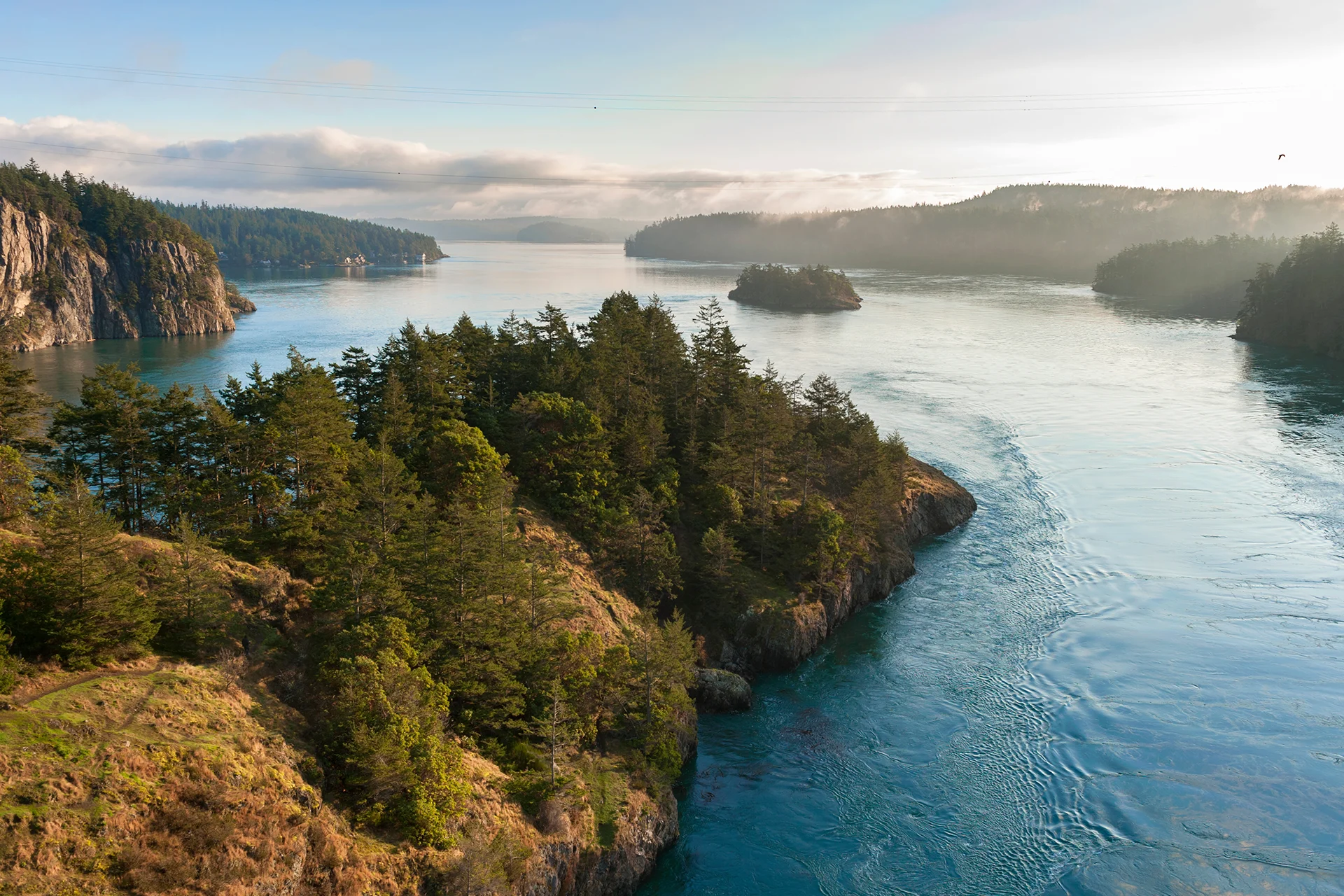 Blue waters of Deception Pass winding between rocky, evergreen-covered islands in Washington state.